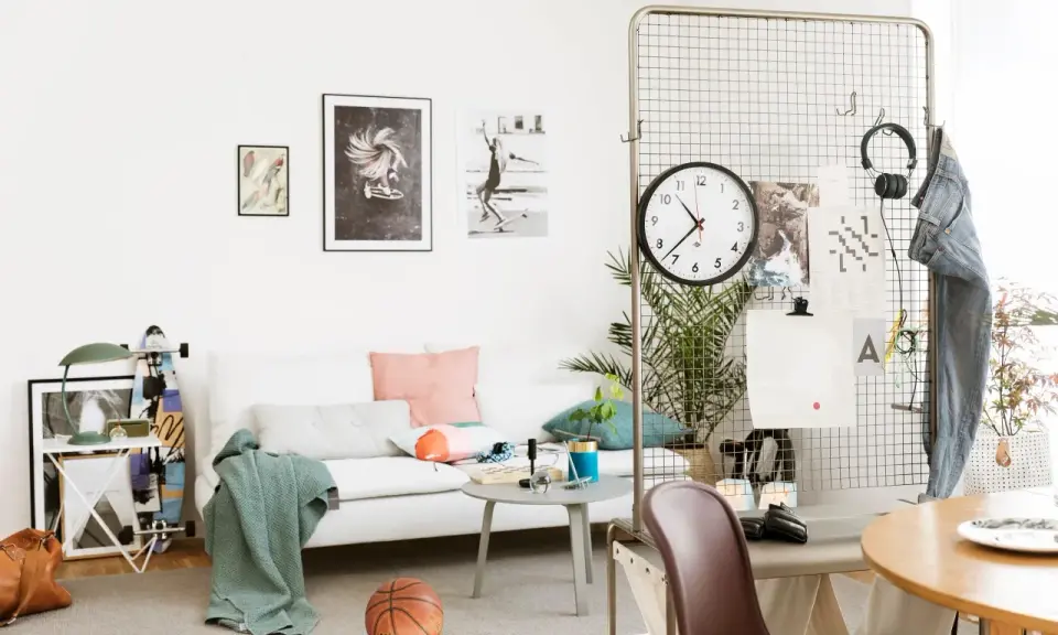 En avslappnad inredning hemma med vit soffa, konst på väggen, en basketboll och en skateboard. En stor klocka hänger på ett metallgaller.
