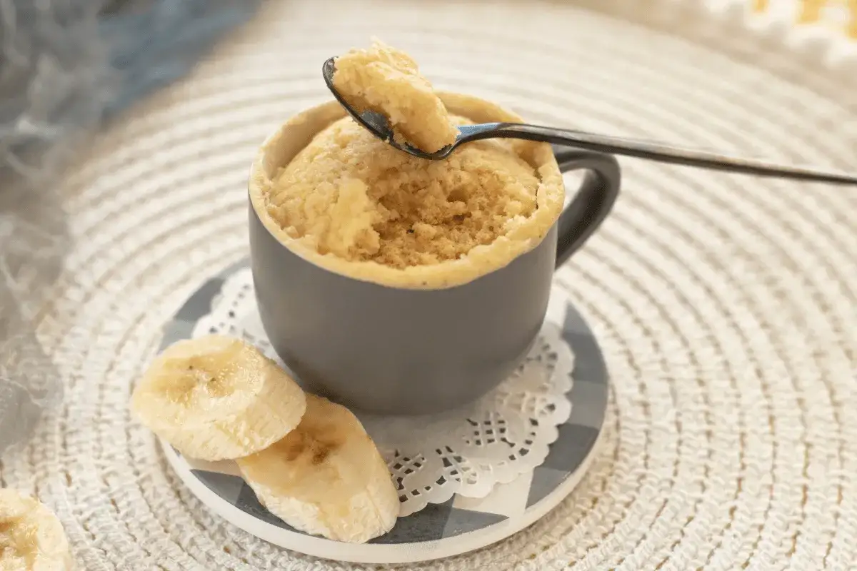 En fluffig mugcake proteinpulver med bananskivor. En sked lyfter en bit av den läckra kakan.
