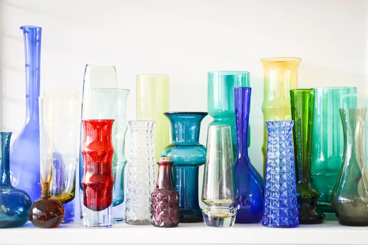 En samling färgglada glasvaser, som dyrgripar på loppis, i olika former och storlekar.