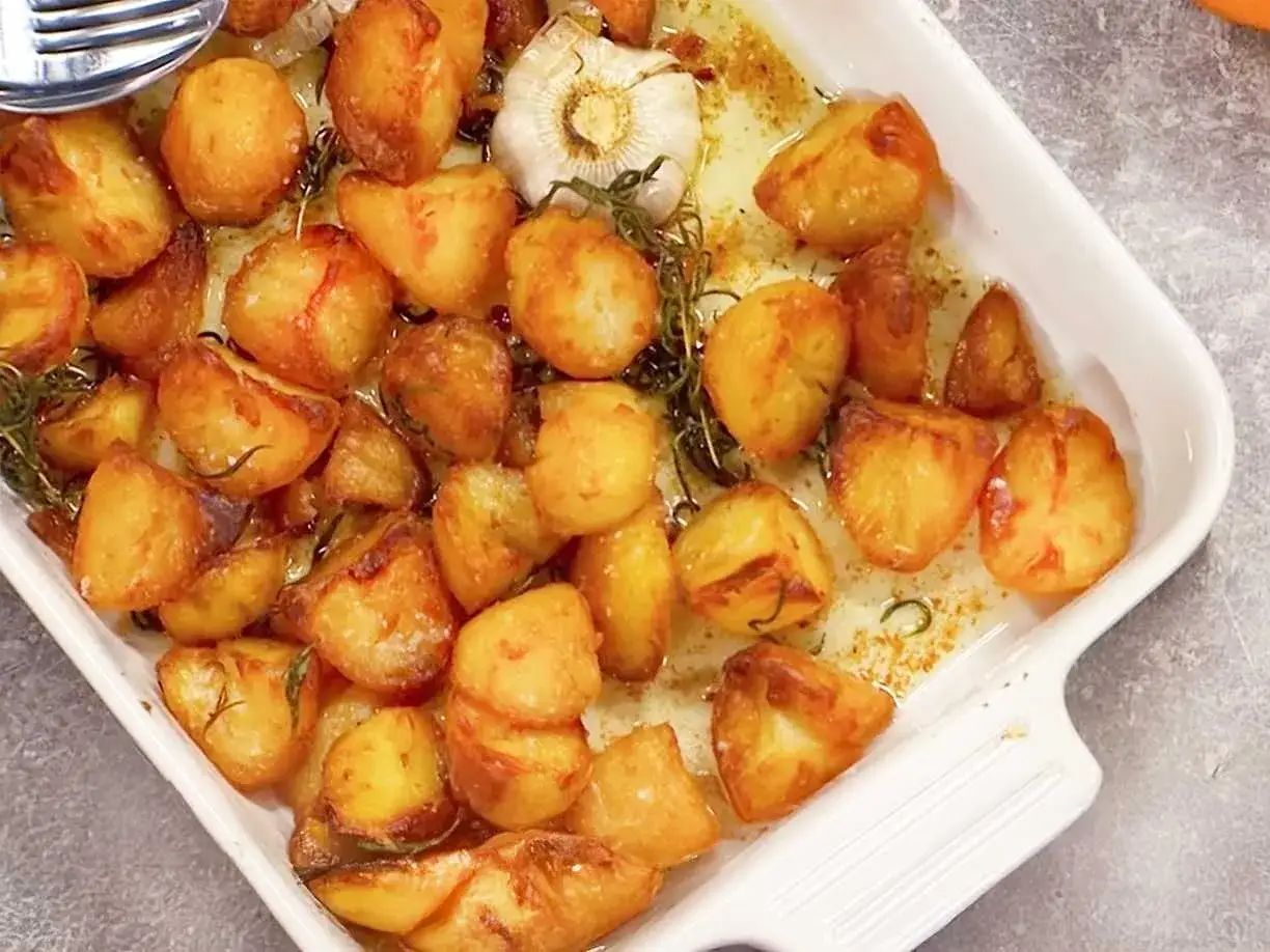 Ugnsrostad potatis i en vit form, gyllene och krispiga, med vitlök och rosmarin. Perfekt tillbehör!