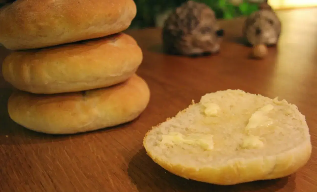 Nybakade tekakor, ett recept som ger fluffigt bröd. En halv tekaka med smör ligger framför en stapel.