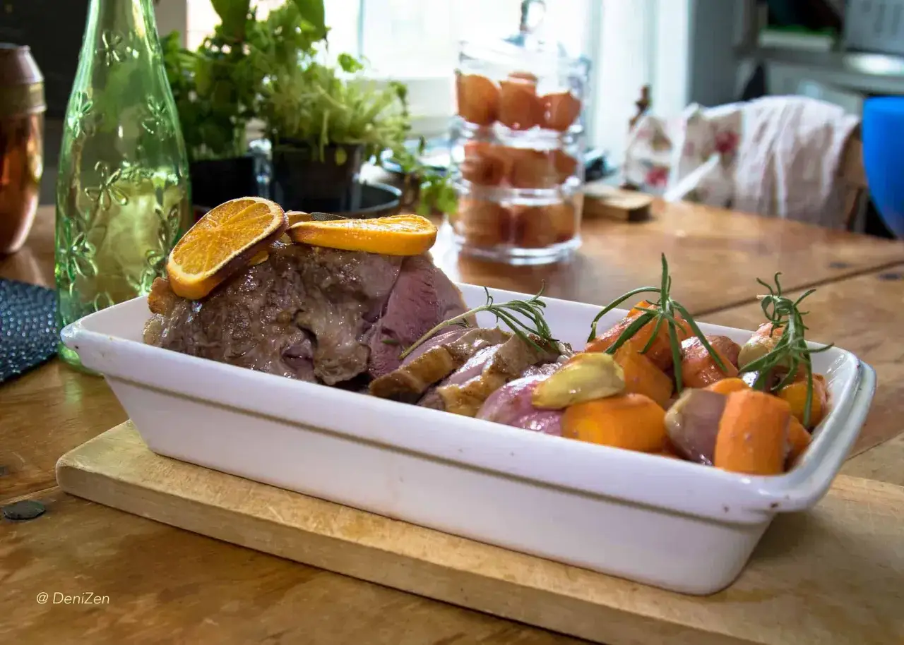 En saftig lammstek i ugn, skivad och serverad med rostade rotfrukter och apelsinskivor.