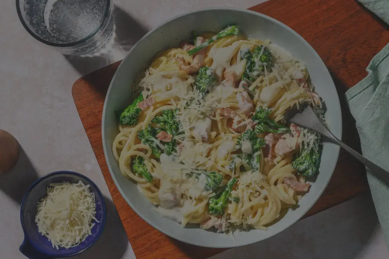En skål med krämig pasta, broccoli och bacon. En klassisk carbonara som ser utsökt ut, toppad med riven ost.