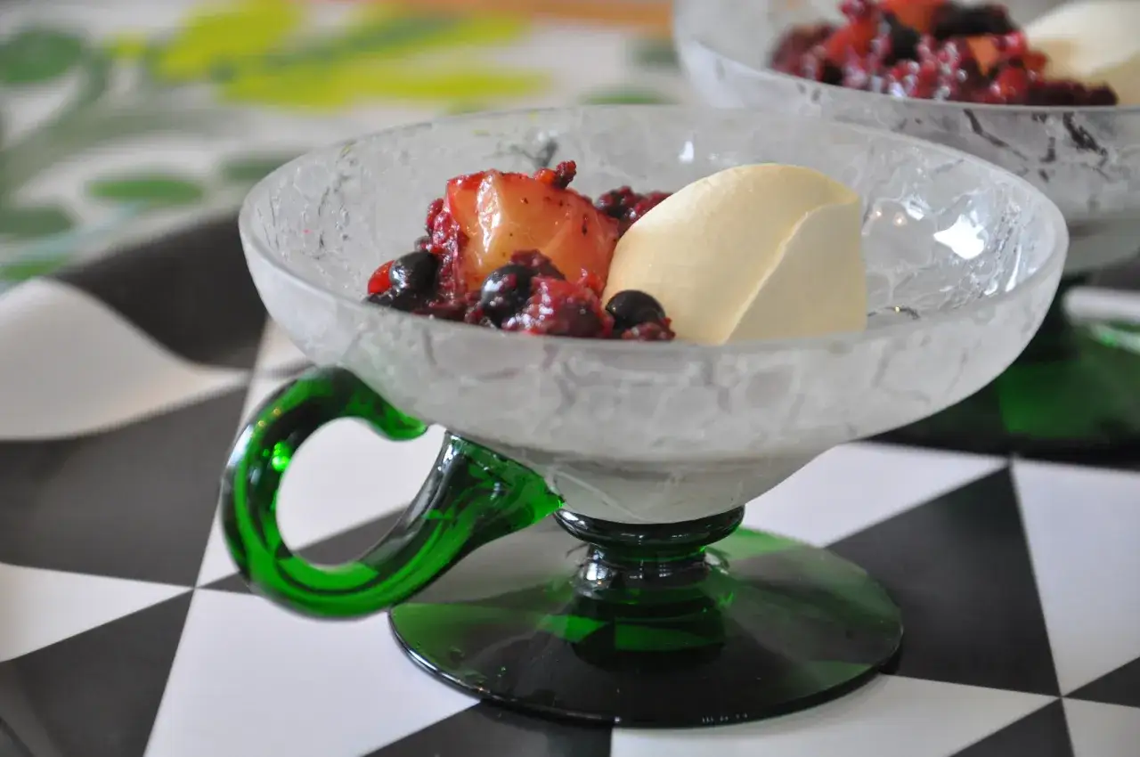 Enkel dessert med bär och frukt i en vacker glasskål med grönt fot.