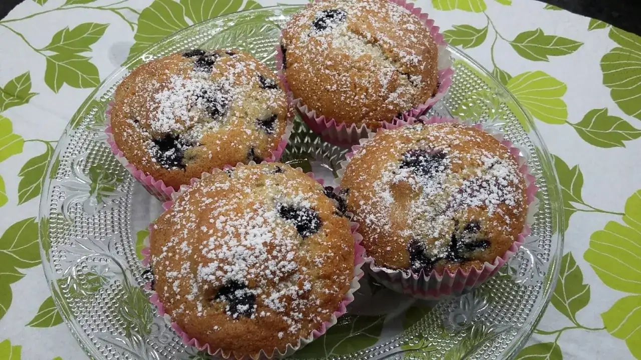 Fyra fluffiga glutenfria muffins med blåbär, pudrade med florsocker, serverade på ett vackert fat.