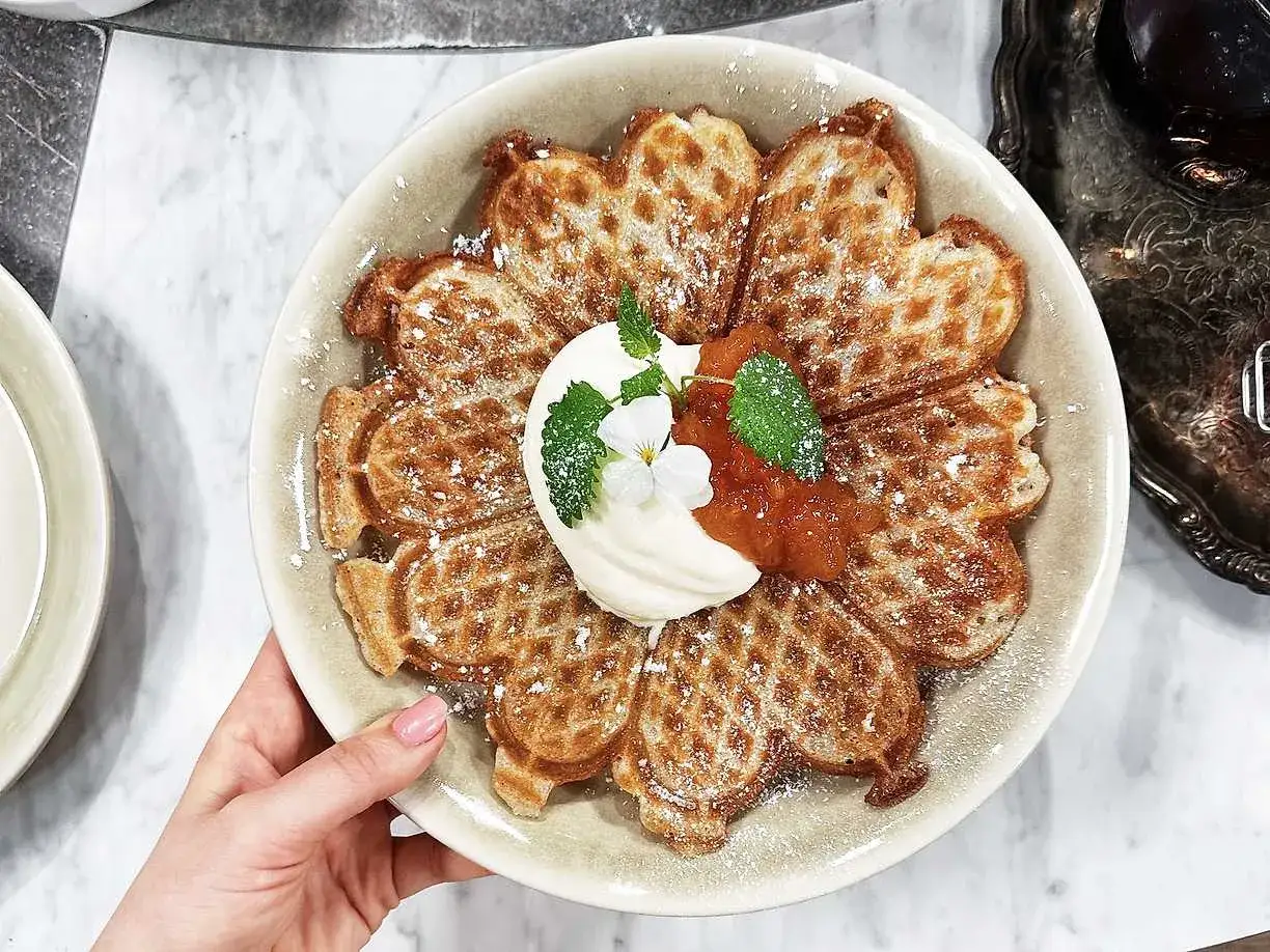 En vacker blomma av glutenfria våfflor, toppad med vispgrädde, sylt och mynta. Perfekt för en fika!