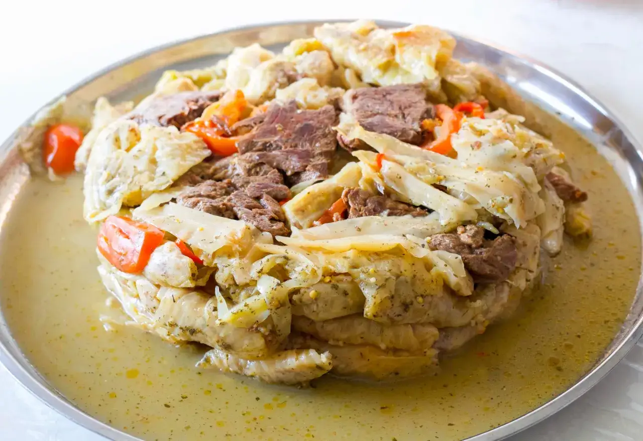 Kåldolmar recept på en stor plåt. Kåldolmarna är fyllda med kött och serveras i en buljong med tomatbitar.
