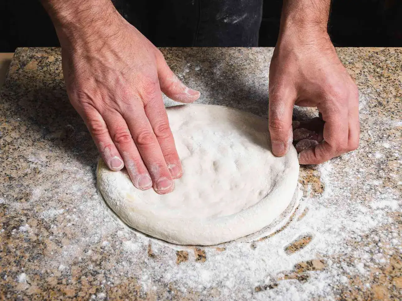 Händer formar en snabb pizzadeg på ett mjölat stenbord.