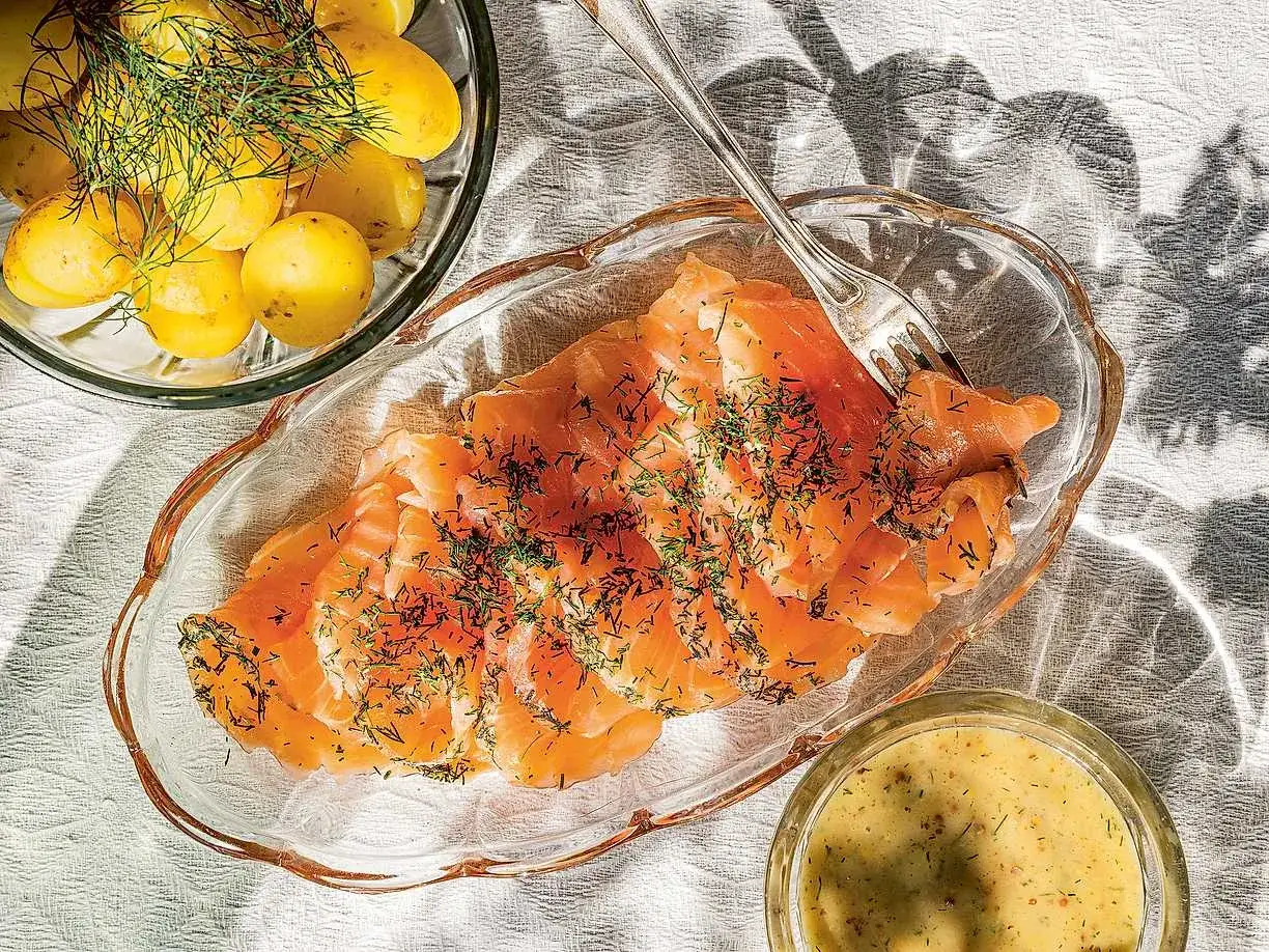 Gravlaxsås recept: Skivad gravad lax med dill, serverad med kokt färskpotatis och en skål med gravlaxsås.
