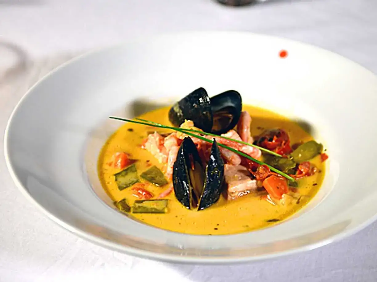 En vacker skål med bouillabaisse, fylld med musslor, räkor och grönsaker i en gyllene buljong. Ett perfekt recept för en lyxig middag.
