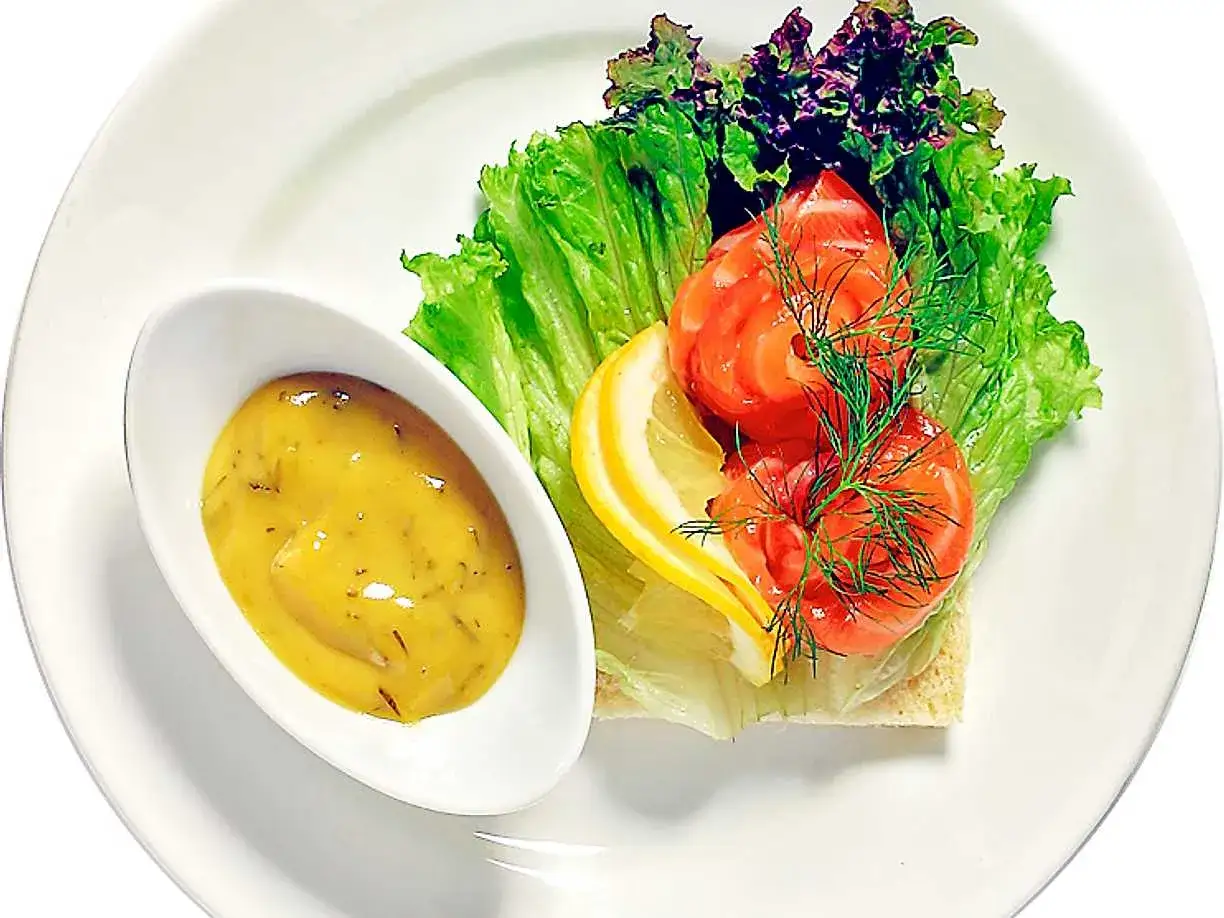 En portion gravad lax med dill och citron på en salladsbädd, serverad med en senapssås.