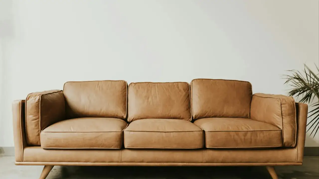 Brun lädersoffa med träben, en del av hållbar inredning. En grön växt syns i bakgrunden.