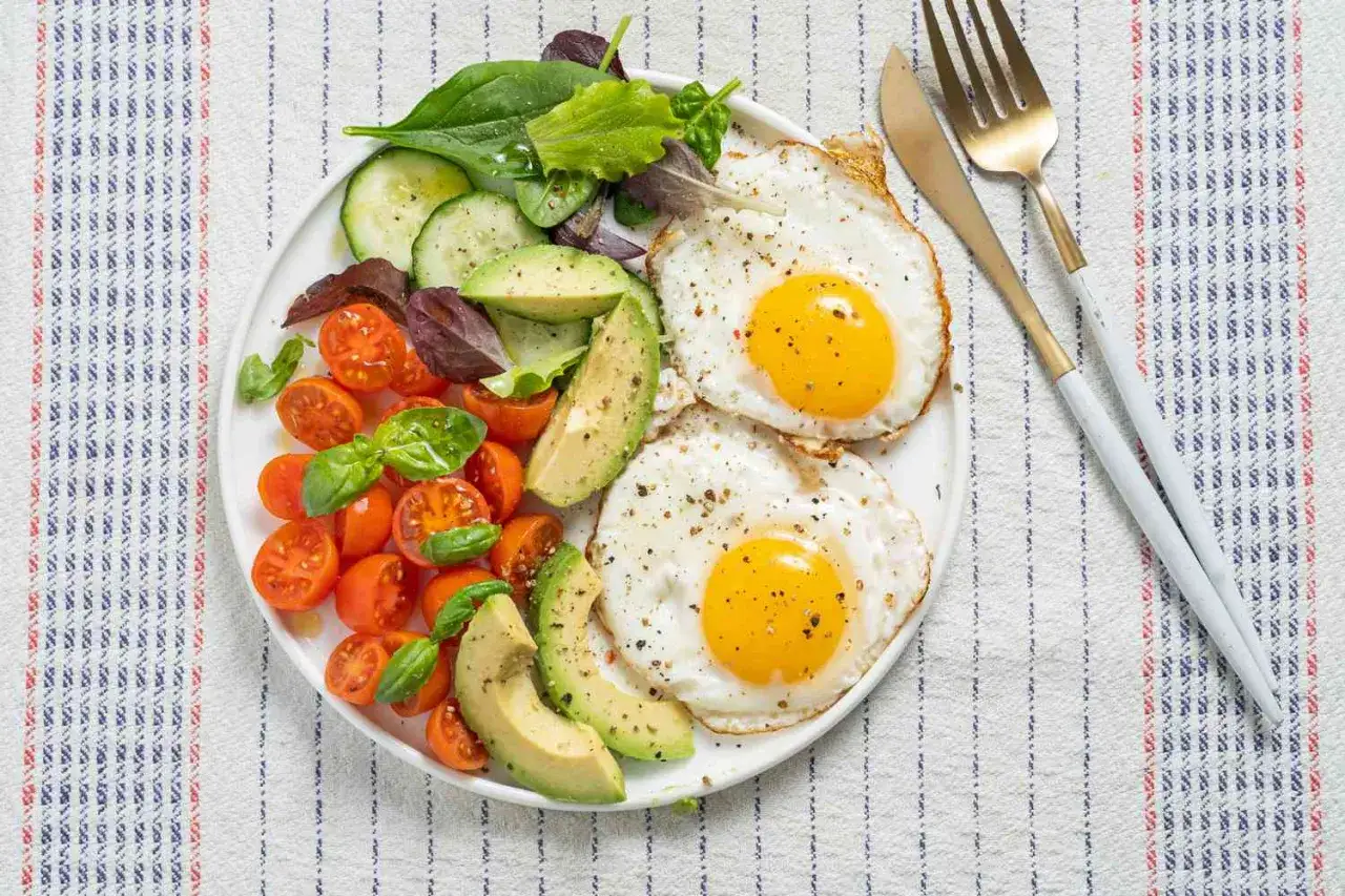 En proteinrik frukost med två stekta ägg, avokado, körsbärstomater och sallad. Perfekt för en energifylld start på dagen.