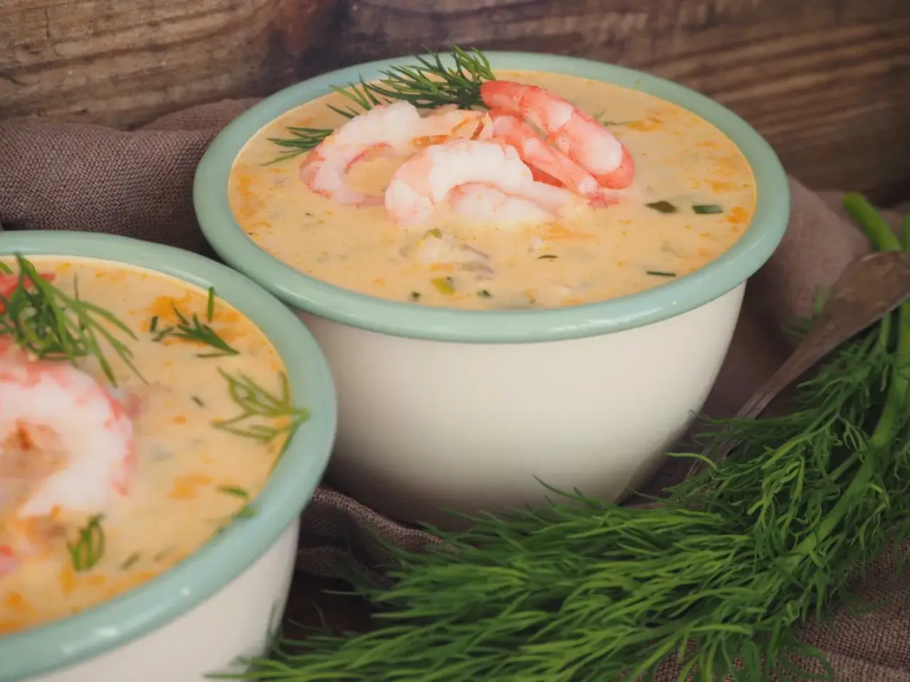Två skålar med krämig fisksoppa, toppad med räkor och dill. Ett perfekt fisksoppa recept för en mysig kväll.