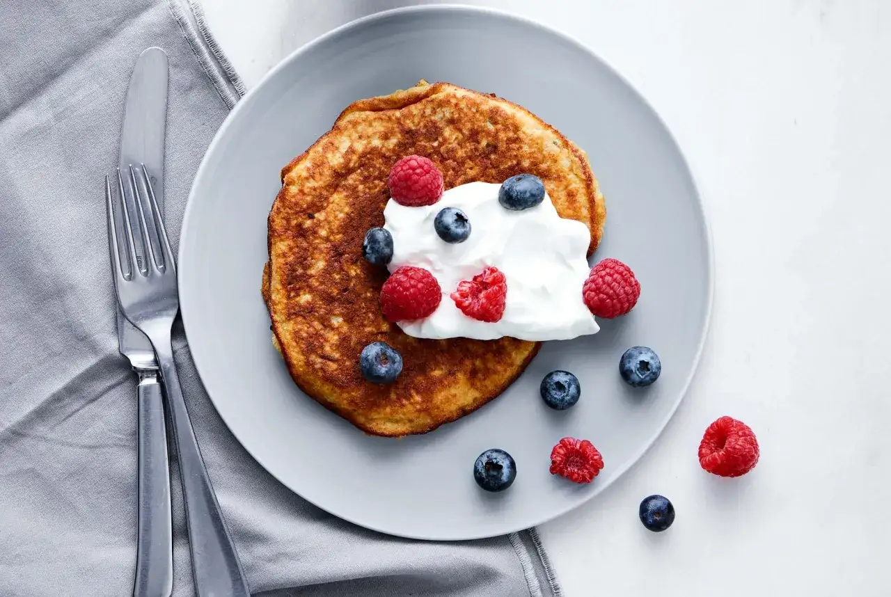En gyllene bananpannkaka toppad med grädde, blåbär och hallon. Ett enkelt bananpannkaka recept för en god frukost.