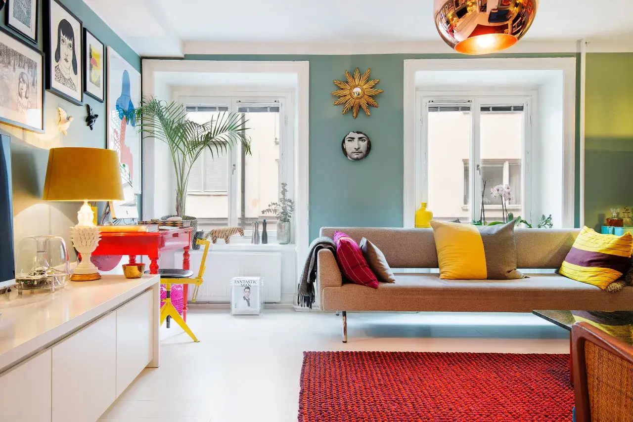 En modern och f&auml;rgstark inredning med konst p&aring; v&auml;ggarna, en bekv&auml;m soffa med kuddar och en r&ouml;d matta. En design klassiker i vardagsrummet.