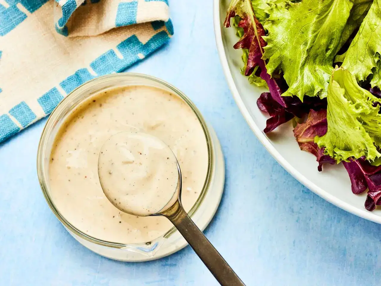 Krämig dressing till sallad i en skål, med en sked som lyfter upp lite av den. Bredvid syns en fräsch sallad.