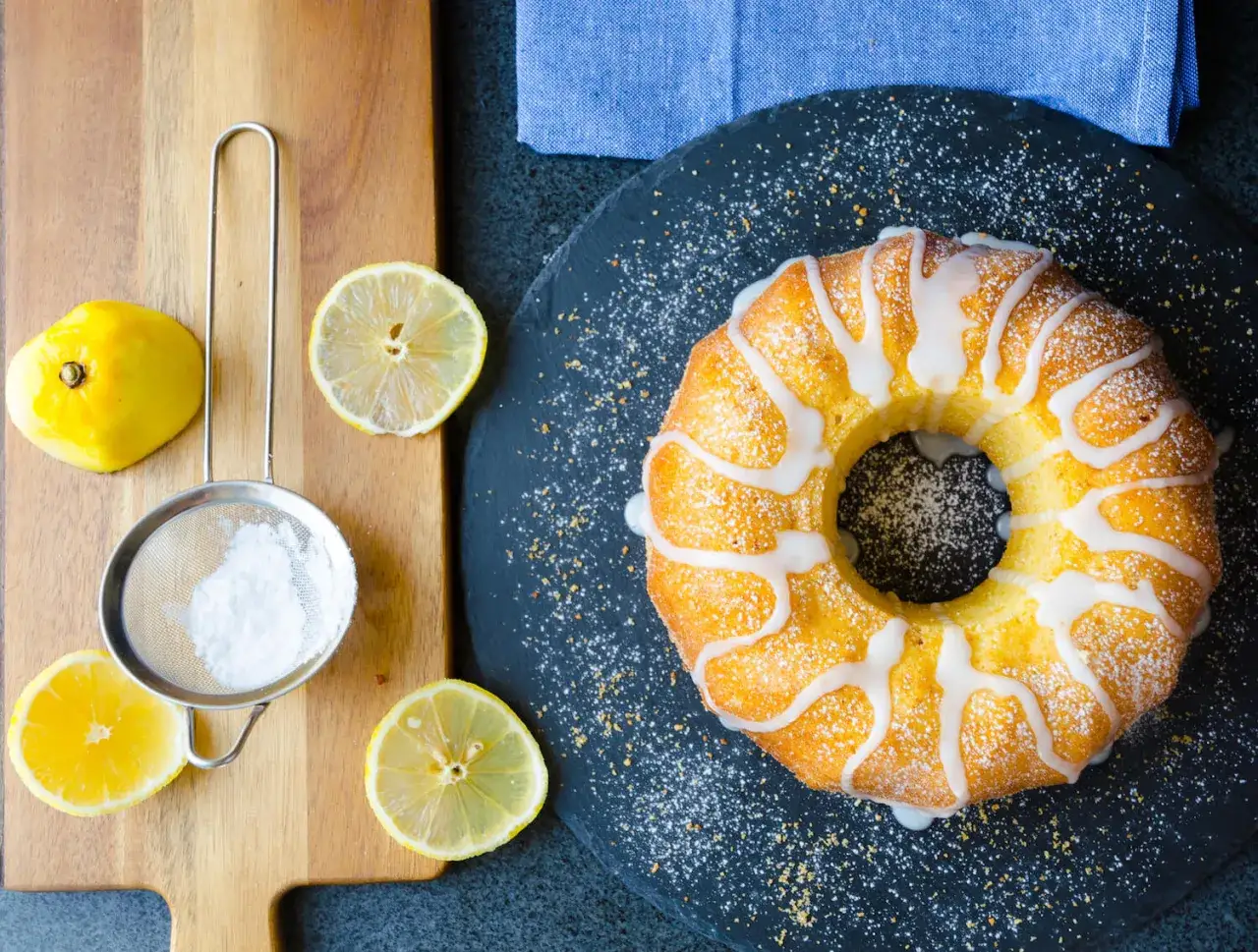 En saftig sockerkaka citron med glasyr och strösocker, omgiven av färska citroner och en sil.