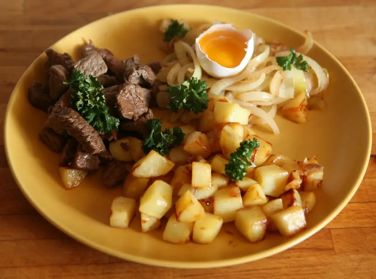 En tallrik med stekt kött, stekt lök, stekt potatis och ett kokt ägg. En klassisk svensk husmanskost som ser utsökt ut.
