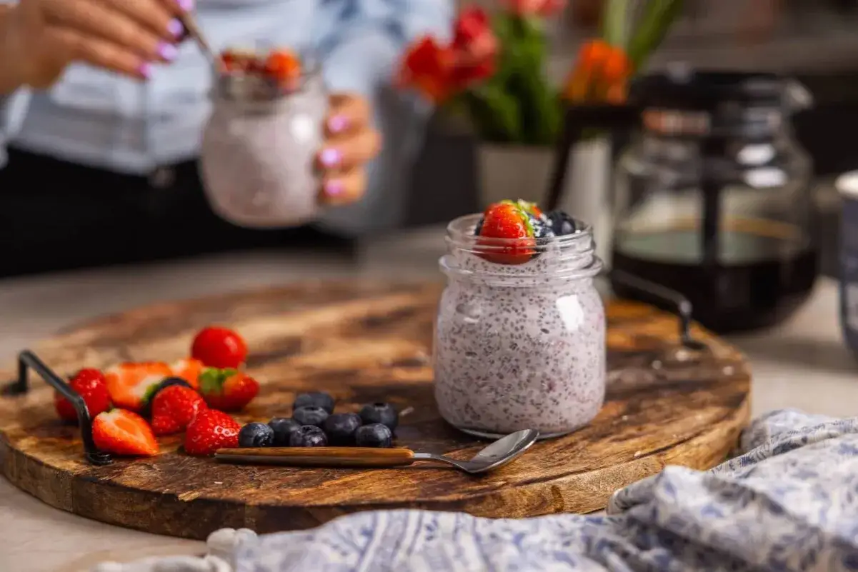 En burk med chia pudding toppad med bär, bredvid färska jordgubbar och blåbär på en träbricka. Ett perfekt chia pudding recept för en hälsosam frukost.