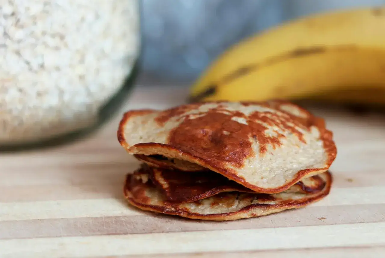 En hög med gyllenbruna, nyttiga pannkakor, gjorda på havre och banan, ligger på en träskärbräda.
