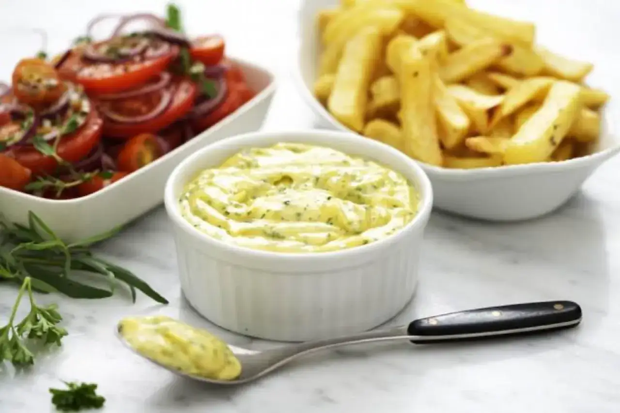 En skål med krämig bearnaisesås, perfekt för pommes frites. Bredvid syns en fräsch tomatsallad. Ett enkelt bearnaise recept.
