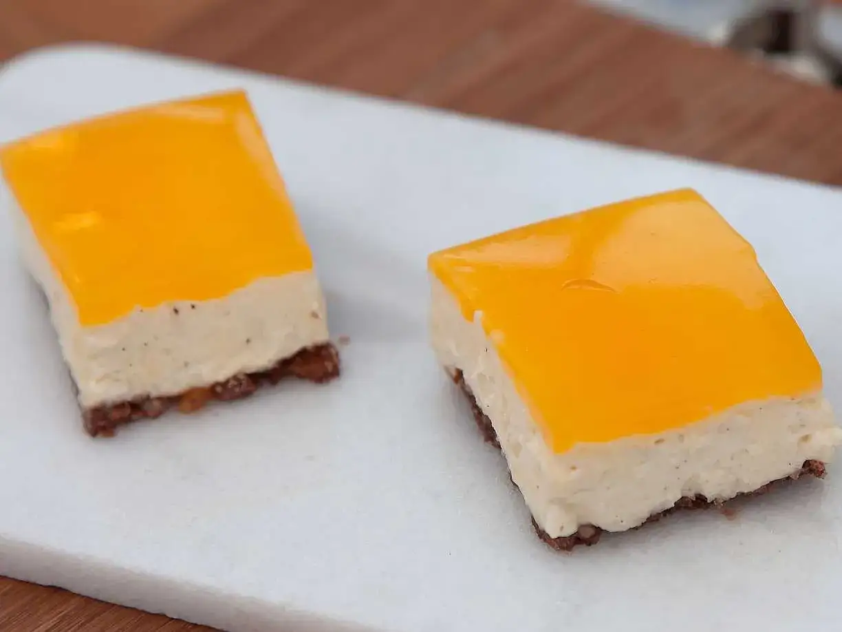 Två läckra budapest bakelser med krämig fyllning och orange gelé på en vit bricka.