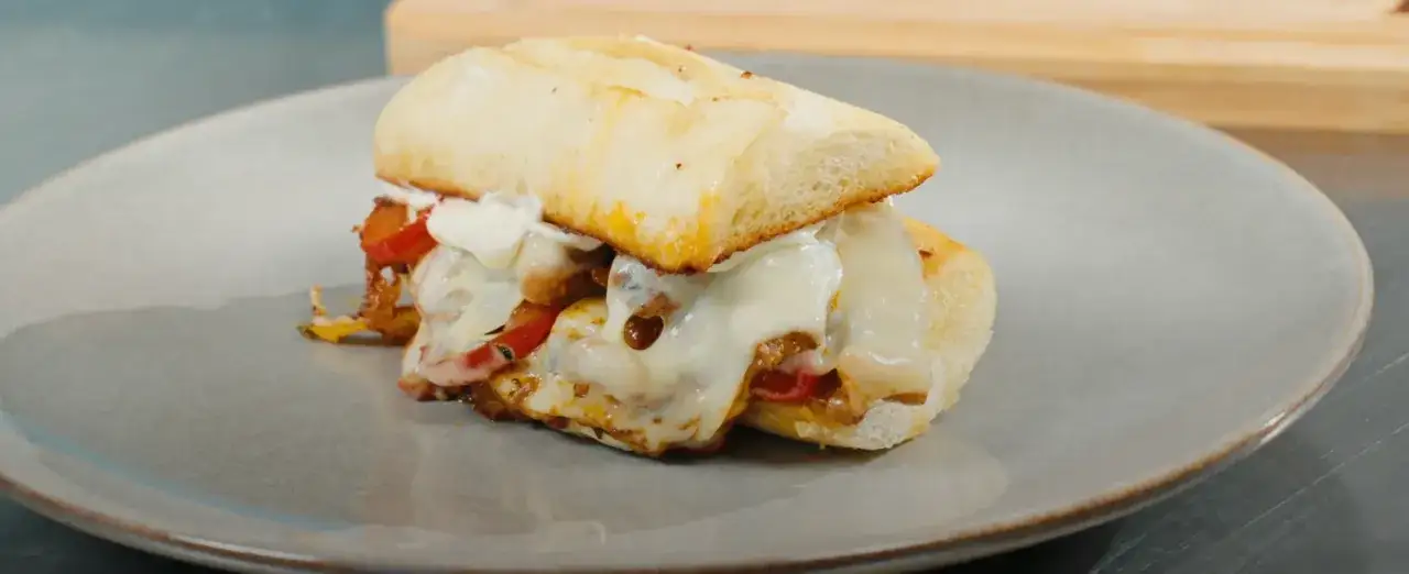 En saftig philly cheese steak med smält ost och paprika på ett mjukt bröd, serverad på en grå tallrik.