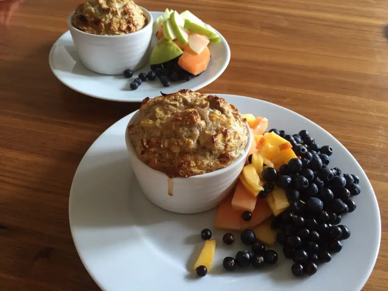 Två portioner baked oats serveras med färsk frukt och bär. En härlig och hälsosam frukost.