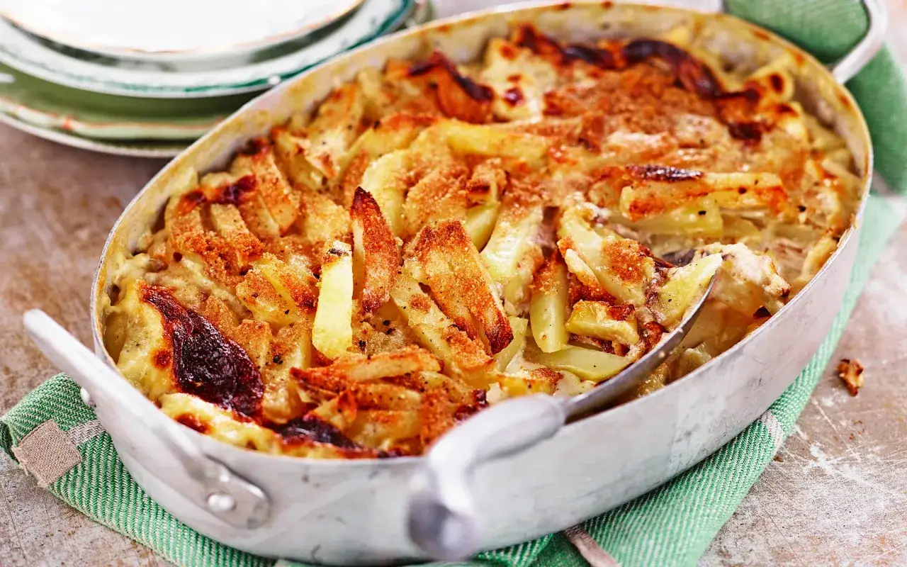 En gyllene Janssons frestelse i en ugnsform, med potatisstavar och en krämig sås.