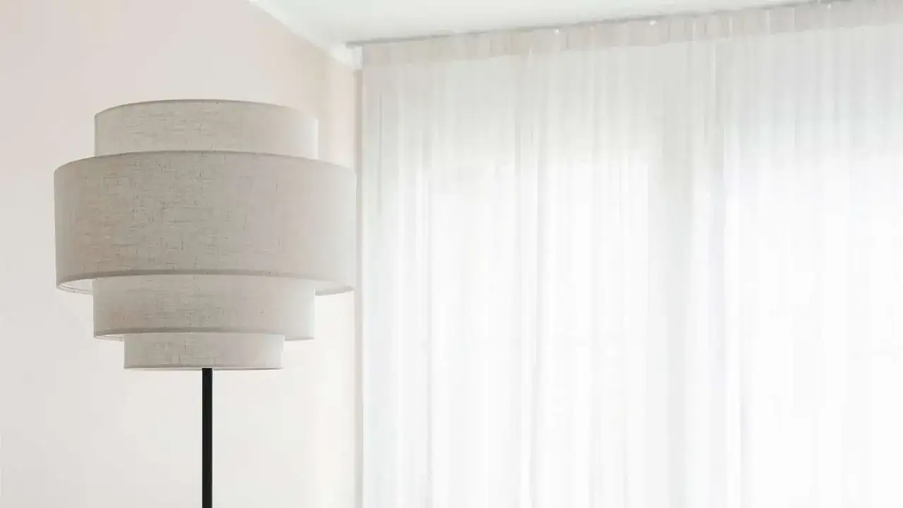 En elegant lampa med flera skärmar står framför en vit, böljande gardinkappa och längder som släpper in ljuset.
