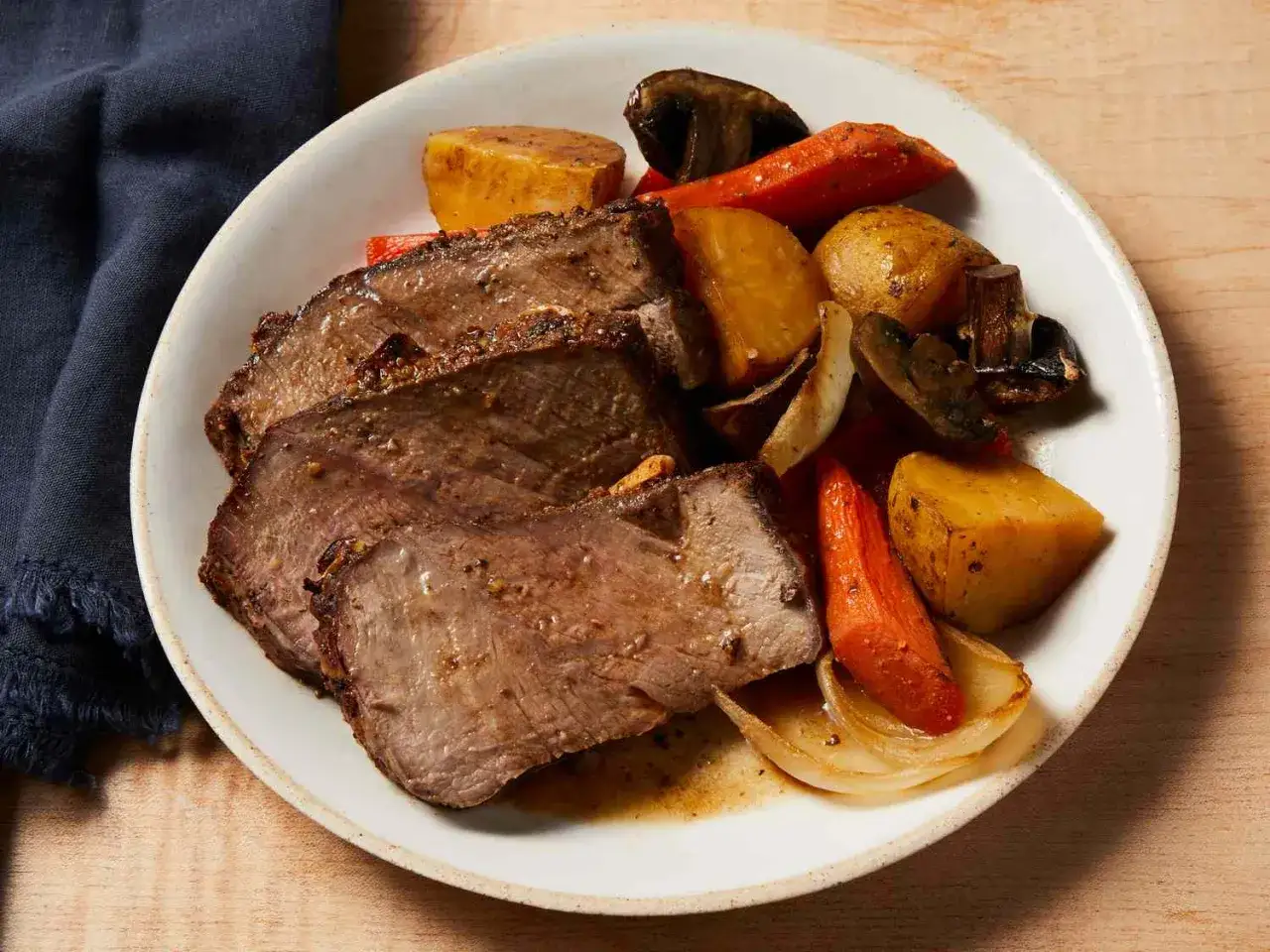 Skivor av saftig ryggbiff i ugn serveras med rostade rotfrukter som potatis, morötter och champinjoner.